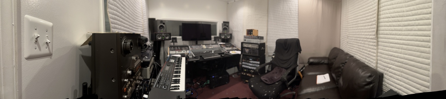 Panoramic view of the Bum-Leg Records recording studio with mixing console, keyboards, rack equipment, monitors, seating, and acoustic treatment